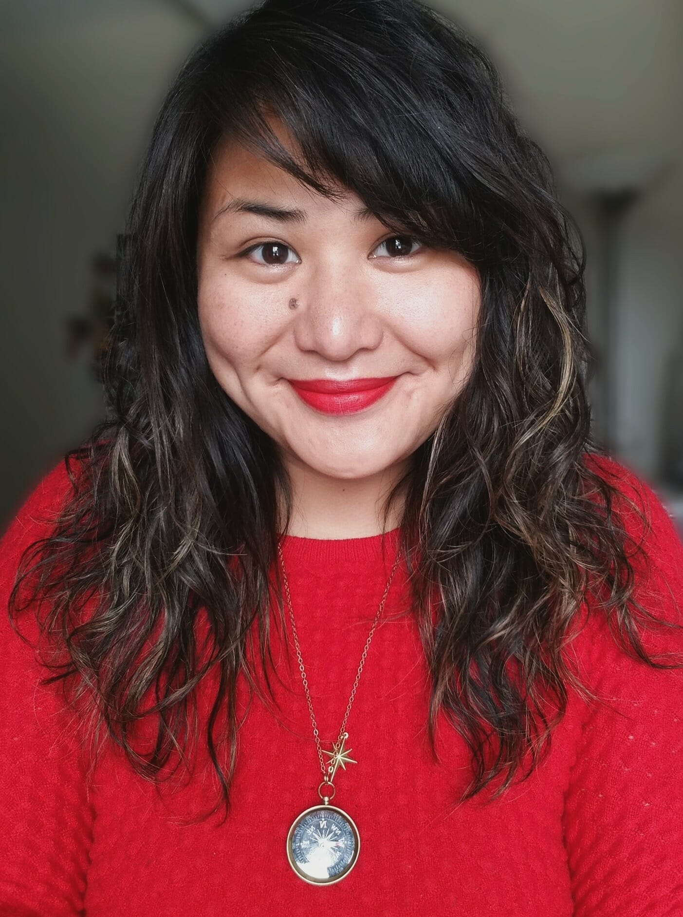 Trish Fontanilla Headshot. Trish is looking straight to camera, and wearing a compass necklace and red sweater.